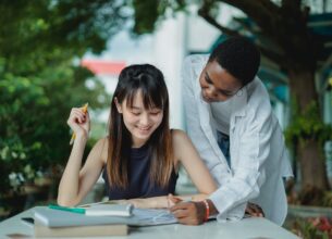 A tutor wearing a white button-up shirt helps a student with her schoolwork