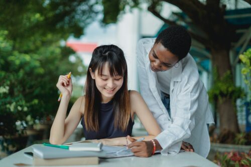 A tutor wearing a white button-up shirt helps a student with her schoolwork