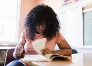 A young student looks over her textbook at her school desk