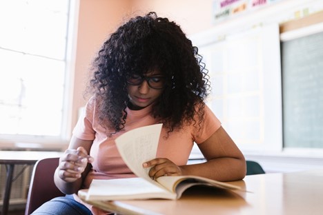 A young student looks over her textbook at her school desk